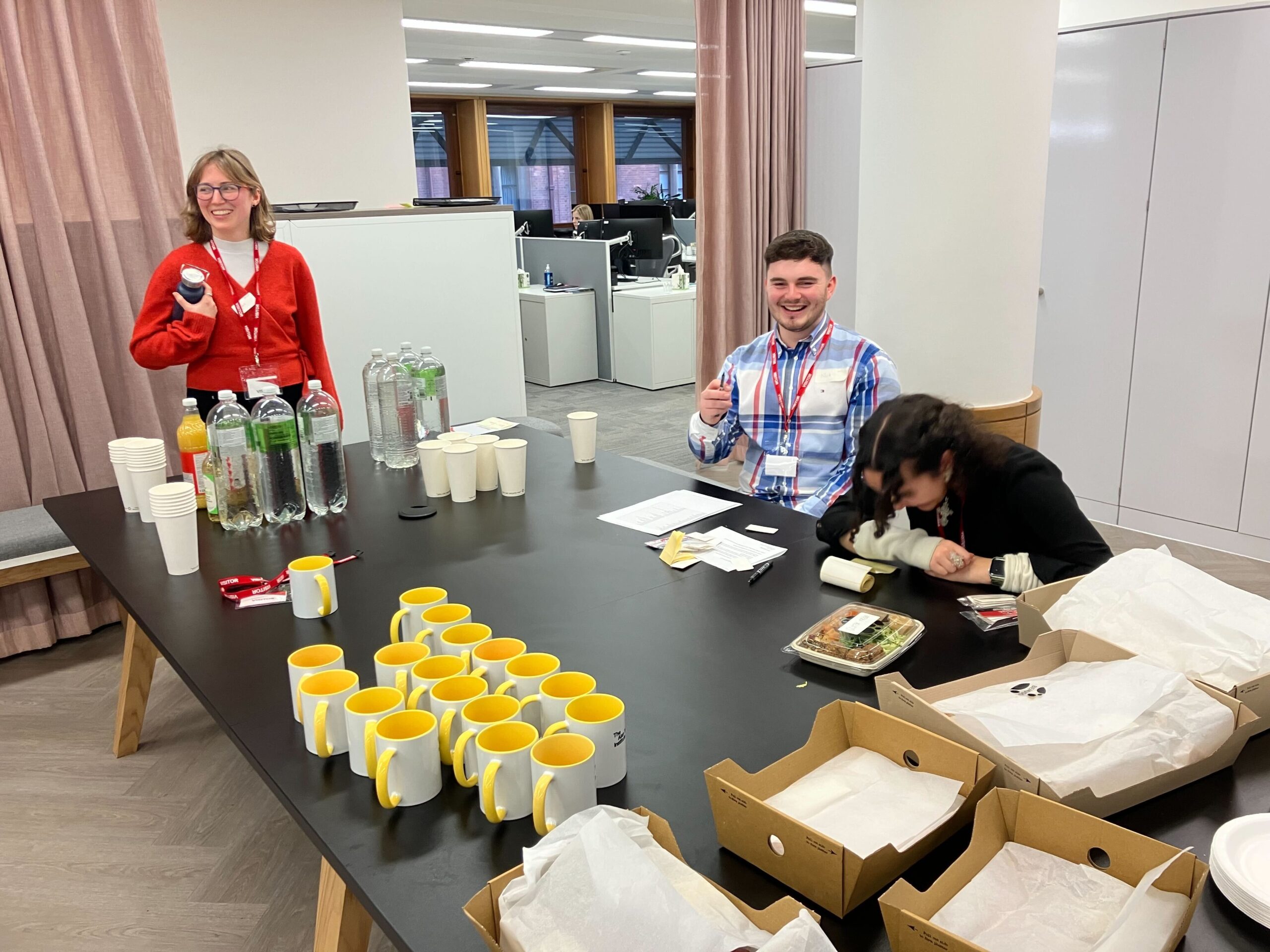 Three members of the We and AI team prepare drinks, name badges and food