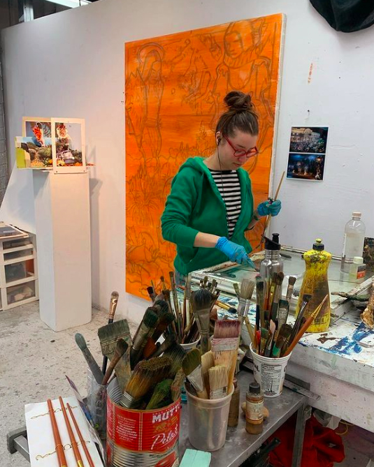 Image of Nicole who shown to be creating art, surrounded by creative tools and equipment like paintbrushes. 