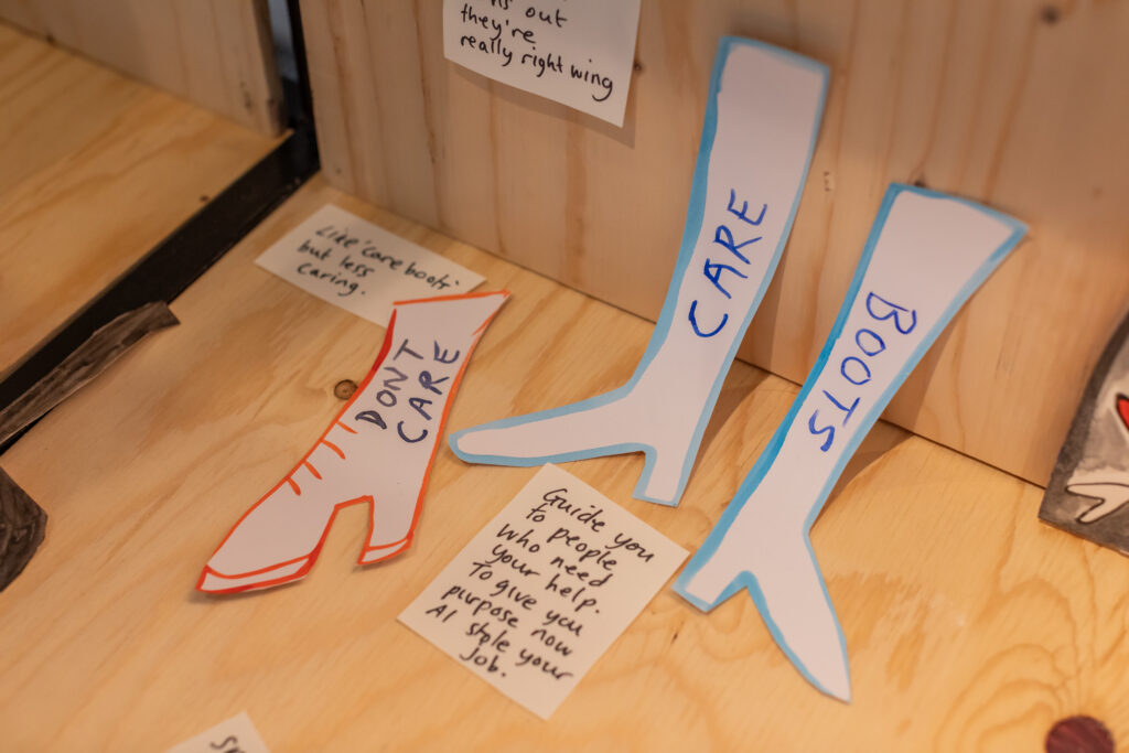 Part of the model's of care exhibition with paper cut into the shape of boots with the words 'boot care', 'care' and 'boots' and other post it notes with individuals reflections