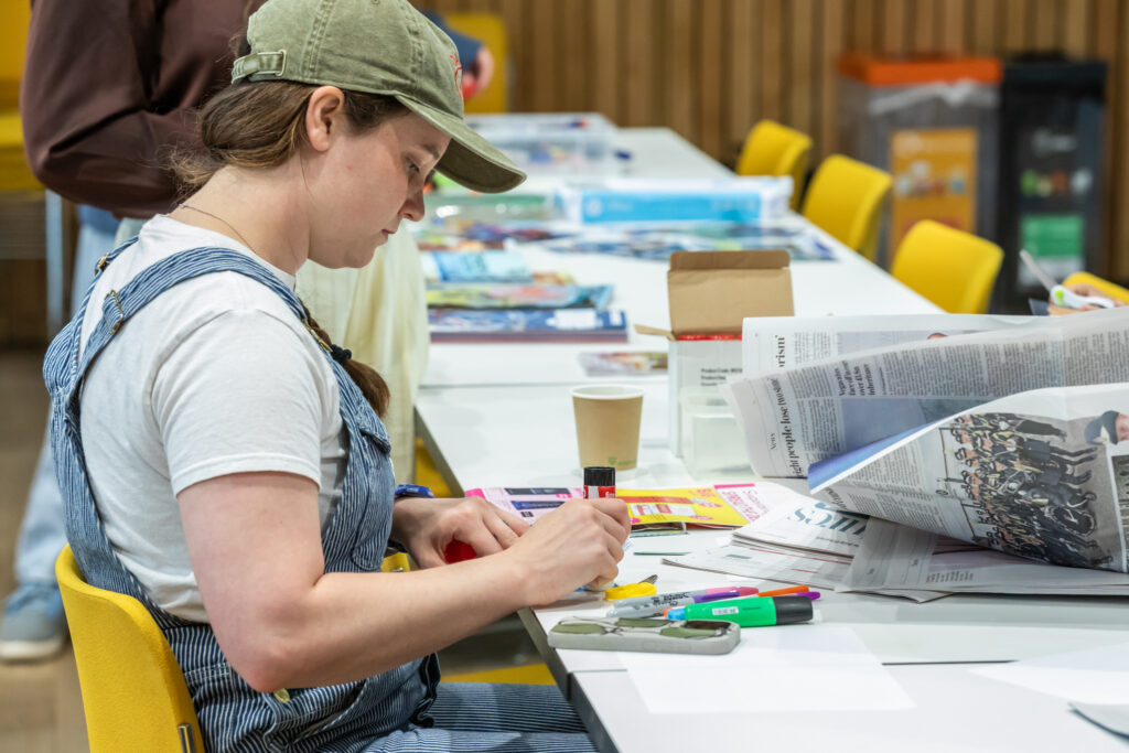 An individual at a table making a zine using various crafting materials like newspapers