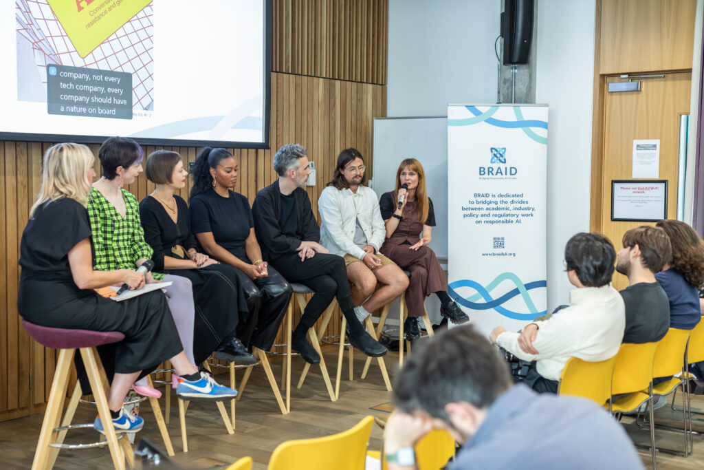 Panelists sat in front of a projector and BRAID banner talking